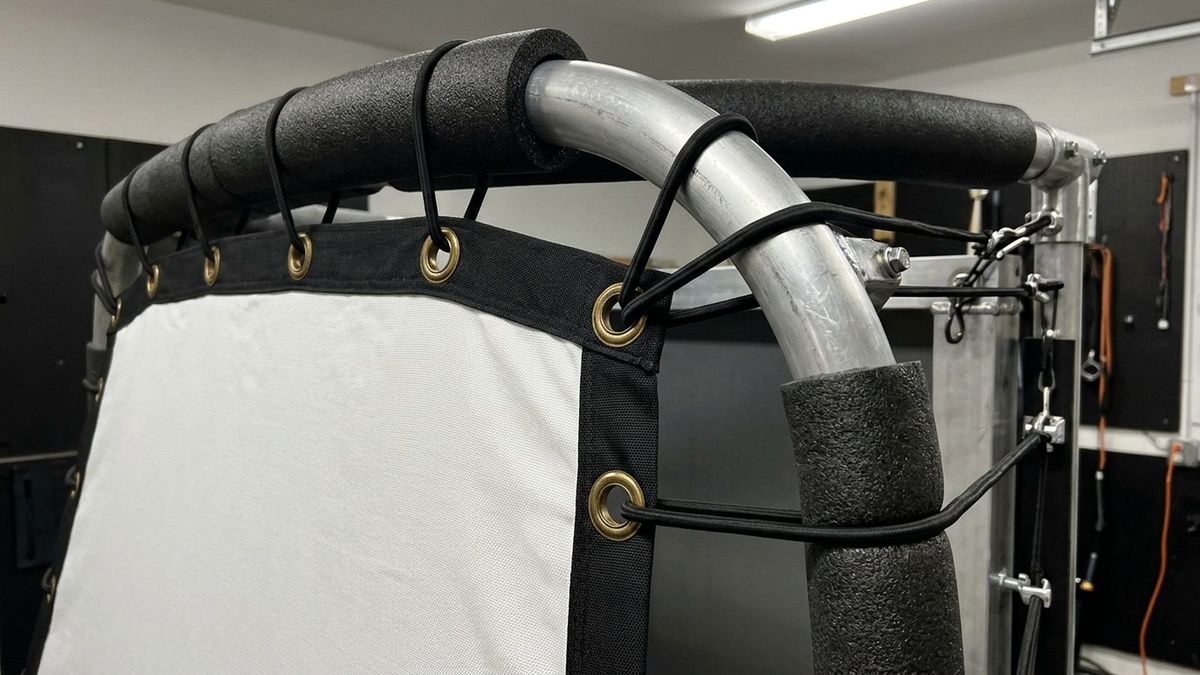 Close-up of curved golf simulator enclosure corner showing bungee cords, brass grommets, and curved aluminum tubing